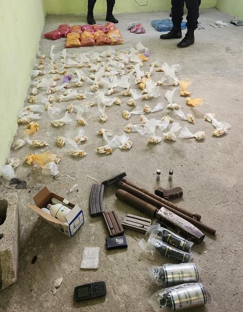 En la imágen se observa la droga, armamento, bombas lacrimógenas y un teléfono en el suelo mientras las autoridades realizan diligencias. (Foto: PNC)
