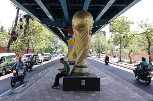 Un hombre iraní está sentado bajo un trofeo de la Copa del Mundo exhibido debajo de un puente en Teherán.