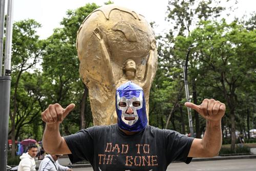 Un vendedor ambulante con una máscara tradicional de lucha libre mexicana, posa frente a una réplica gigante del trofeo del Mundial en Ciudad de México.