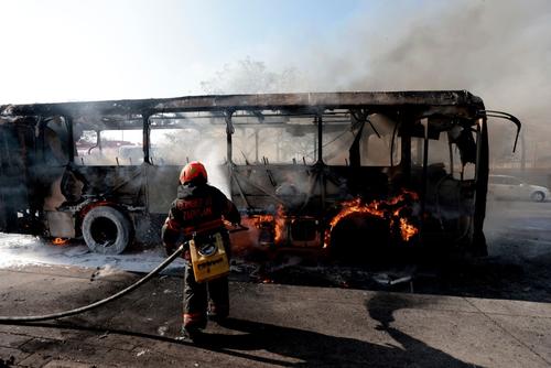 Un bombero extingue un autob&uacute;s en llamas, incendiado por grupos del crimen organizado en respuesta a un operativo en Jalisco. (Foto: AFP / Soy502)