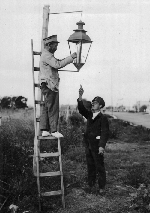 Momento en que un farolero se dispone a encender la luminaria, pues comienza a caer la noche. (Foto: Wikimedia Commons)