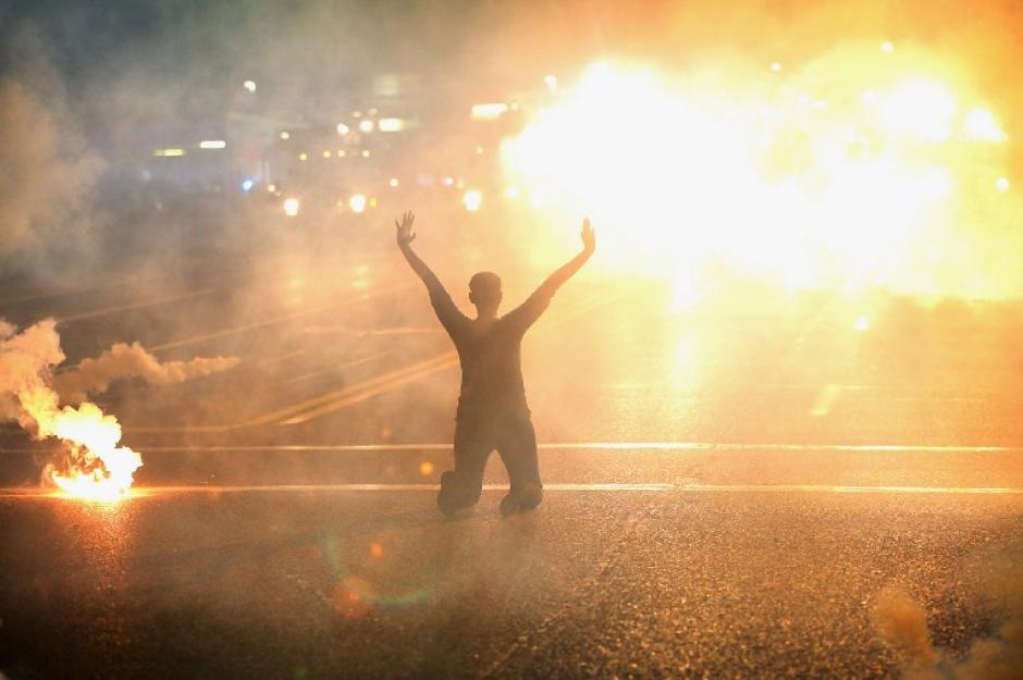 Gas lacrim&oacute;geno se observa y una mujer arrodillada en la calle con las manos al aire, despu&eacute;s de una manifestaci&oacute;n por el asesinato de un adolescente en Ferguson, Missouri. (Foto: AFP)&nbsp;