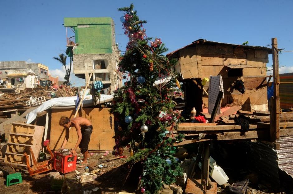 Un hombre recopila materiales recuperables entre los escombros de las casas destruidas en Tacloban, provincia de Leyte, en Filipinas, frente a un &aacute;rbol de Navidad erigido entre el desastre que dej&oacute; el tif&oacute;n Haiyan. (Foto: AFP)&nbsp;