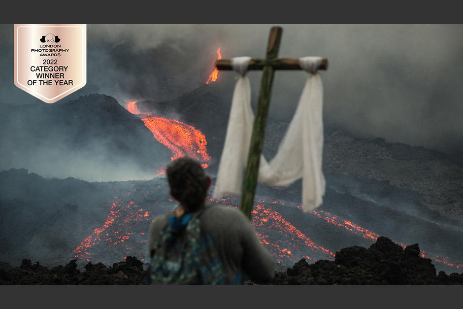 El guatemalteco captó como una mujer sostiene una cruz de madera y reza frente al volcán Pacaya, rezando para que la lava pare y no llegue a su hogar, el 5 de mayo de 2021 en San Vicente Pacaya. (Foto: Esteban Biba/EFE)