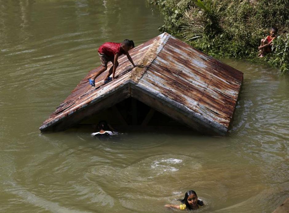 Una ni&ntilde;a filipina se encarama a un tejado y otras nadan tras la crecida de un r&iacute;o, a consecuencia del tif&oacute;n Hagupit, en la isla de Samar, Filipinas. (Foto: EFE)