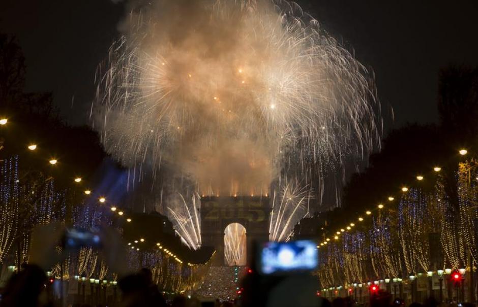 Personas se reunieron en los Campos El&iacute;seos para las celebraciones de A&ntilde;o Nuevo en Francia; al fondo fuegos pirot&eacute;cnicos adornan el Arco de Triunfo. (Foto: Ian Langsdon/EFE)