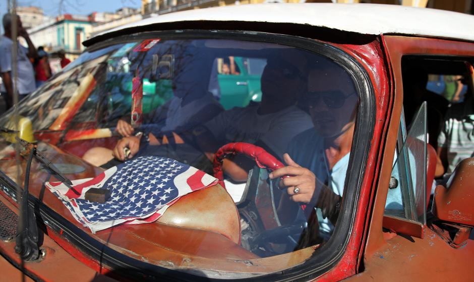 Un hombre maneja en Cuba su taxi con una bandera de Estados Unidos, los ciudadanos celebran. (Foto: EFE)&nbsp;
