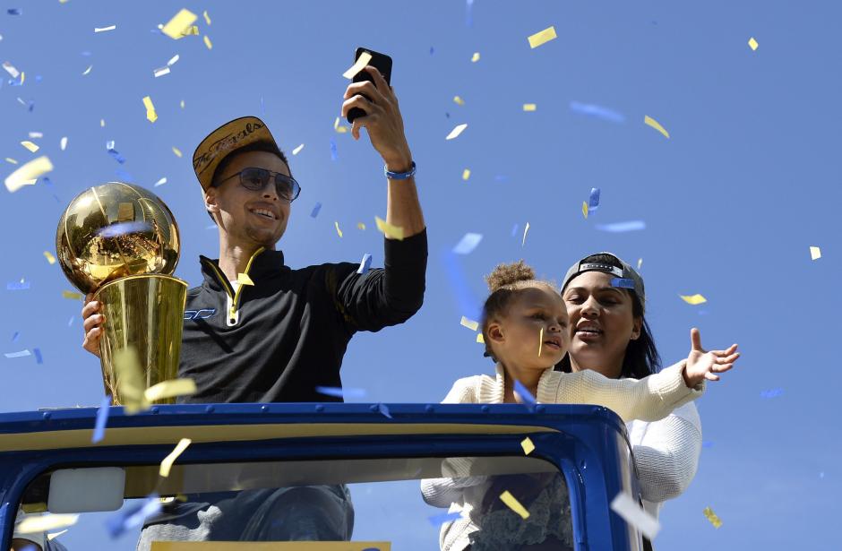 El base de los Golden State Warriors Stephen Curry hace fotograf&iacute;as con su m&oacute;vil junto a su mujer, Ayesha, y su hija, Rilery, durante el desfile protagonizado por su equipo, campe&oacute;n de la NBA, que recorre en autob&uacute;s varias calles de la ciudad de Oakland, California, Estados Unidos, el viernes 19 de junio de 2015. Los Warrios se hicieron con el t&iacute;tulo tras vencer 4-2 a los Cavaliers de Cleveland durante las Finales de la NBA. (EFE/John G. Mabanglo)