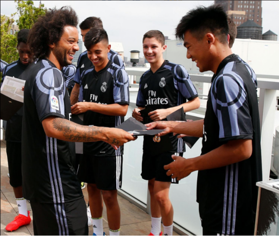 Marcelo le ense&ntilde;a a un joven c&oacute;mo se hace el saludo con James. (RealMadrid.com)