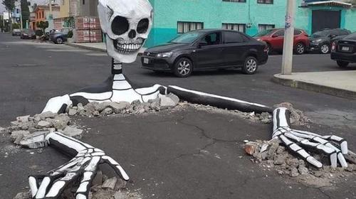 Vecinos aprovechan baches y colocan calaveras gigantes